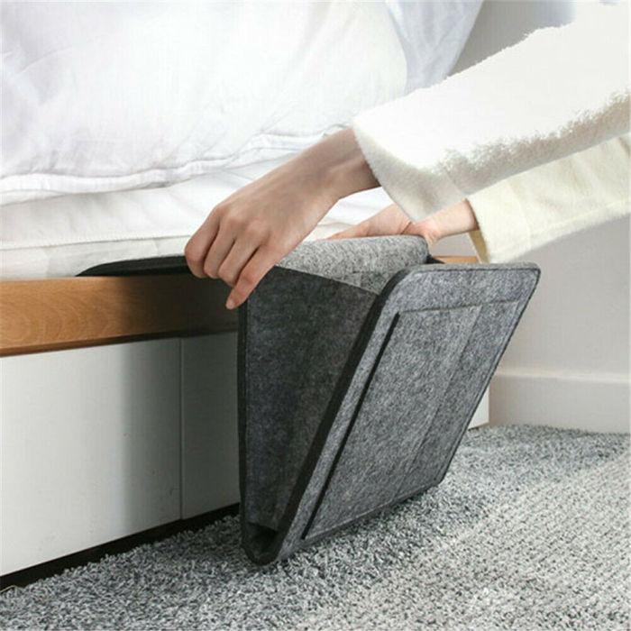 Een dame hangt de grijze BedCaddy aan de zijkant van een wit bed.
