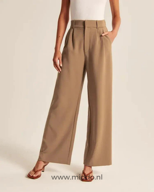 Een dame showt de Bruine wijde pantalon met 2 steekzakken en heeft bruine slippers met hakken aan.